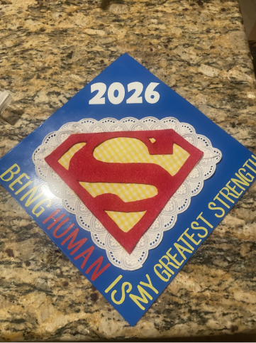 A graduation cap decorated with a Superman symbol and the words “Being human is my greatest strength.”