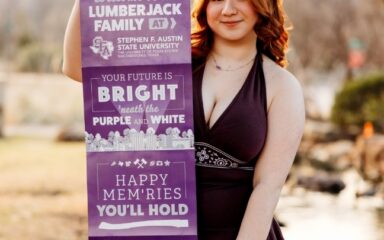 Violet holding a Stephen F. Austin State University welcome banner outdoors.