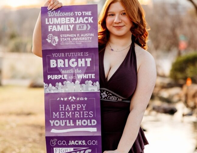 Violet holding a Stephen F. Austin State University welcome banner outdoors.